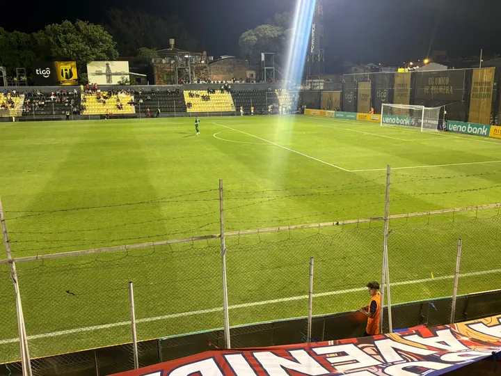 Um gandula espremido entre a grade "coroada" por arames farpados e as placas de publicidade
