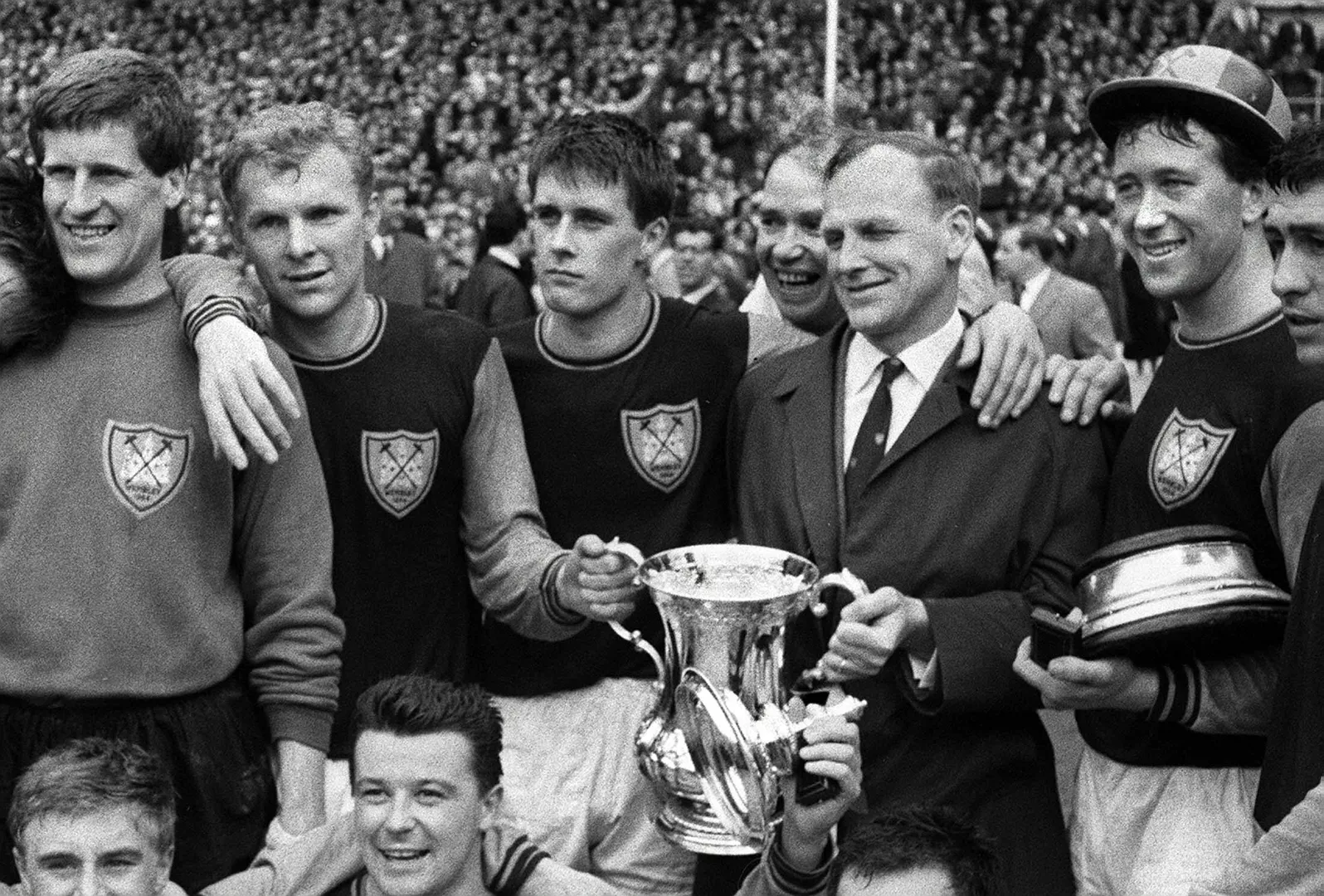 Bobby Moore (o segundo da esquerda &agrave; direita) comemorando o t&iacute;tulo da FA Cup pelo West Ham com o treinador Ron Greenwood (de terno e gravata) (Foto: Imago)